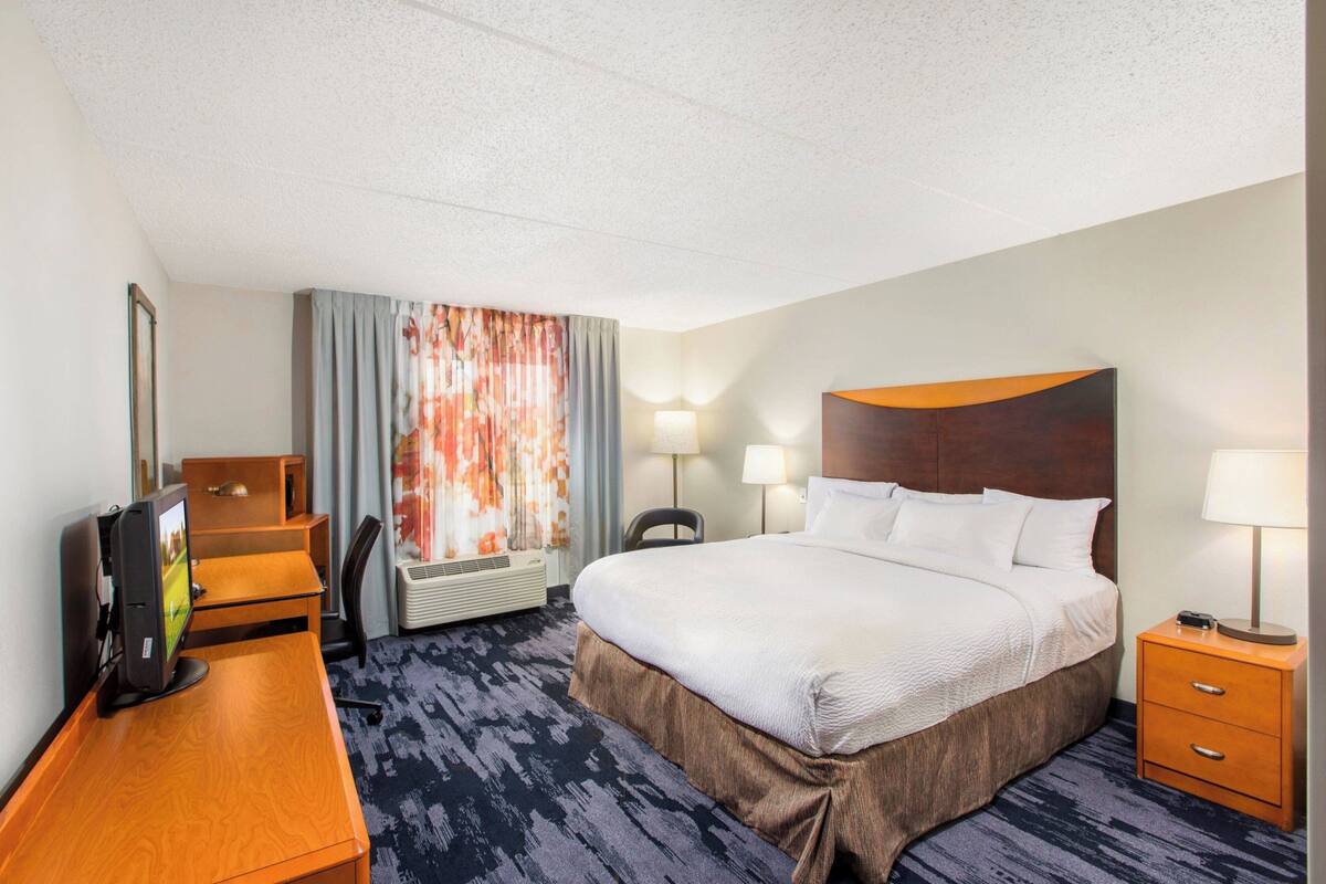 A hotel room with a large bed, a desk with a computer, a chair, and a TV.