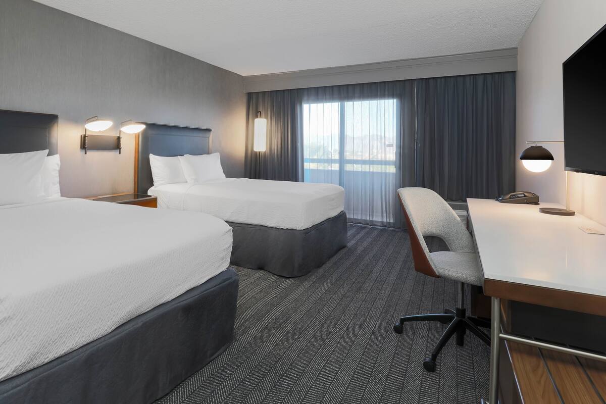 A hotel room with two beds, a desk, and a chair.