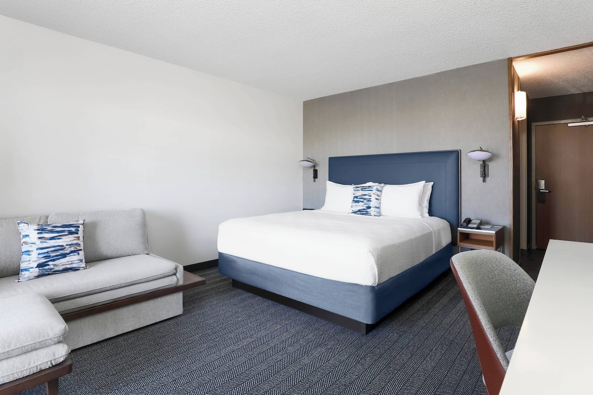 A hotel room with a large bed, a sofa, a desk, and a chair.