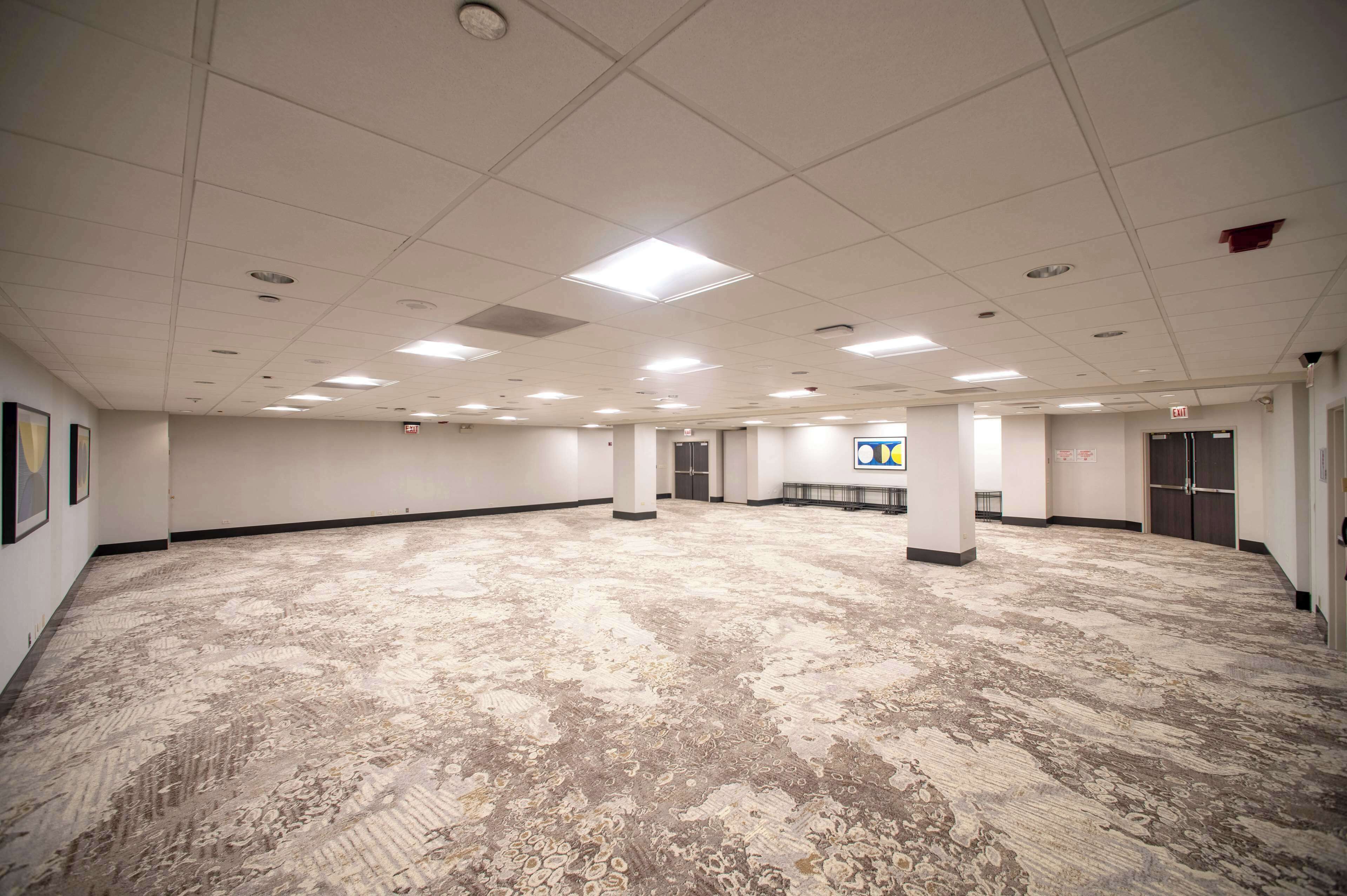 Un salón de conferencias amplio y vacío con alfombra estampada, paredes blancas e iluminación empotrada en el techo.
