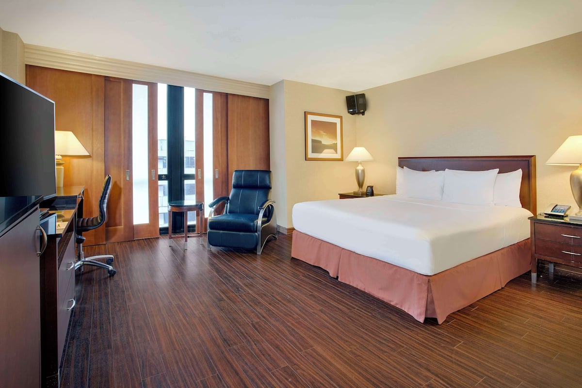 Een hotelkamer met een groot bed, een bureau met stoel, een televisie en een raam met luxaflex.