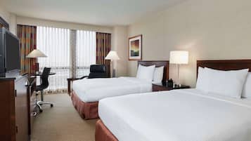 A hotel room with two beds, a desk, a chair, a TV, and two lamps.