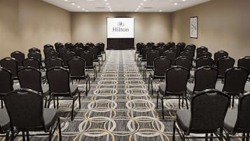 Ein Konferenzraum mit Reihen von Stühlen, einem Teppichboden und einer Projektionsleinwand mit dem Hilton-Logo.