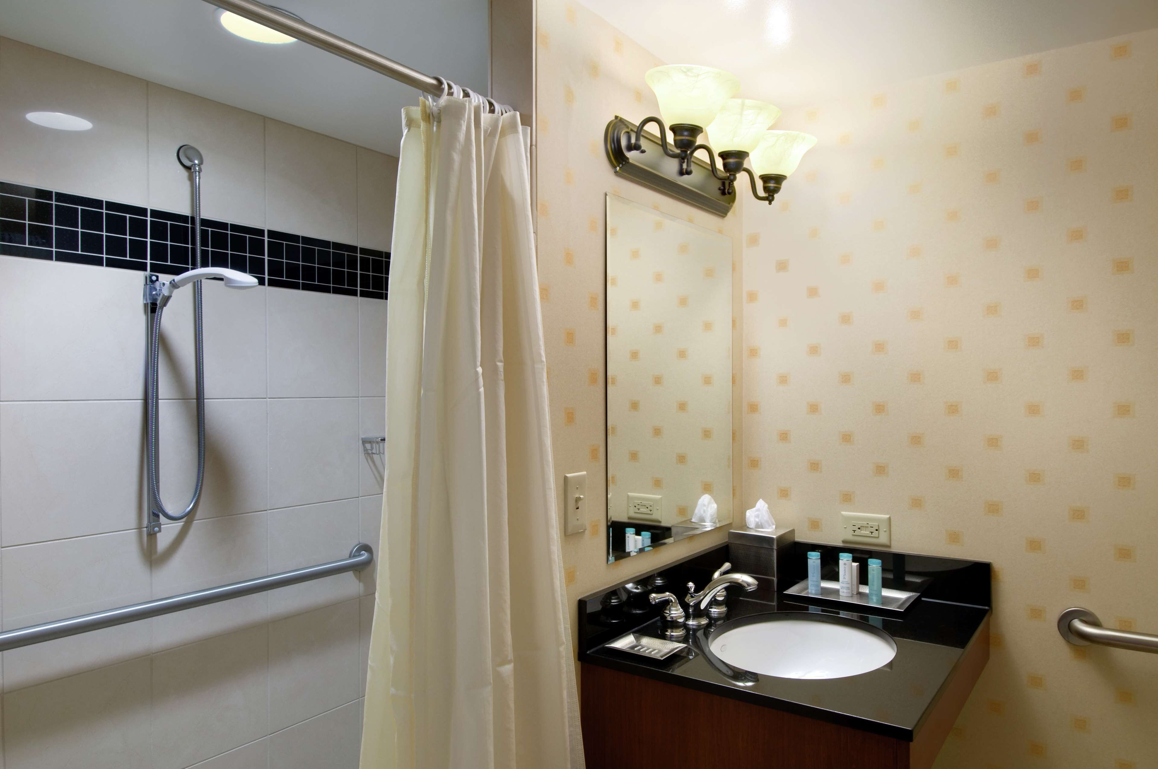 A bathroom with a shower, a sink, a mirror, and a towel rack.