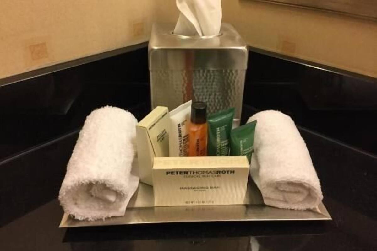Een hotelkamer met een badkamermeubel, een pak tissues, toiletartikelen en twee opgerolde handdoeken.