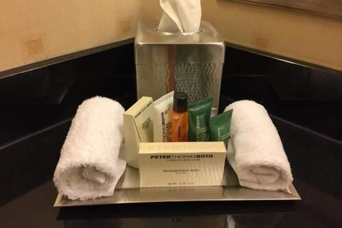 Une chambre d’hôtel avec un meuble-lavabo dans la salle de bain, une boîte de mouchoirs, des articles de toilette et deux serviettes enroulées.