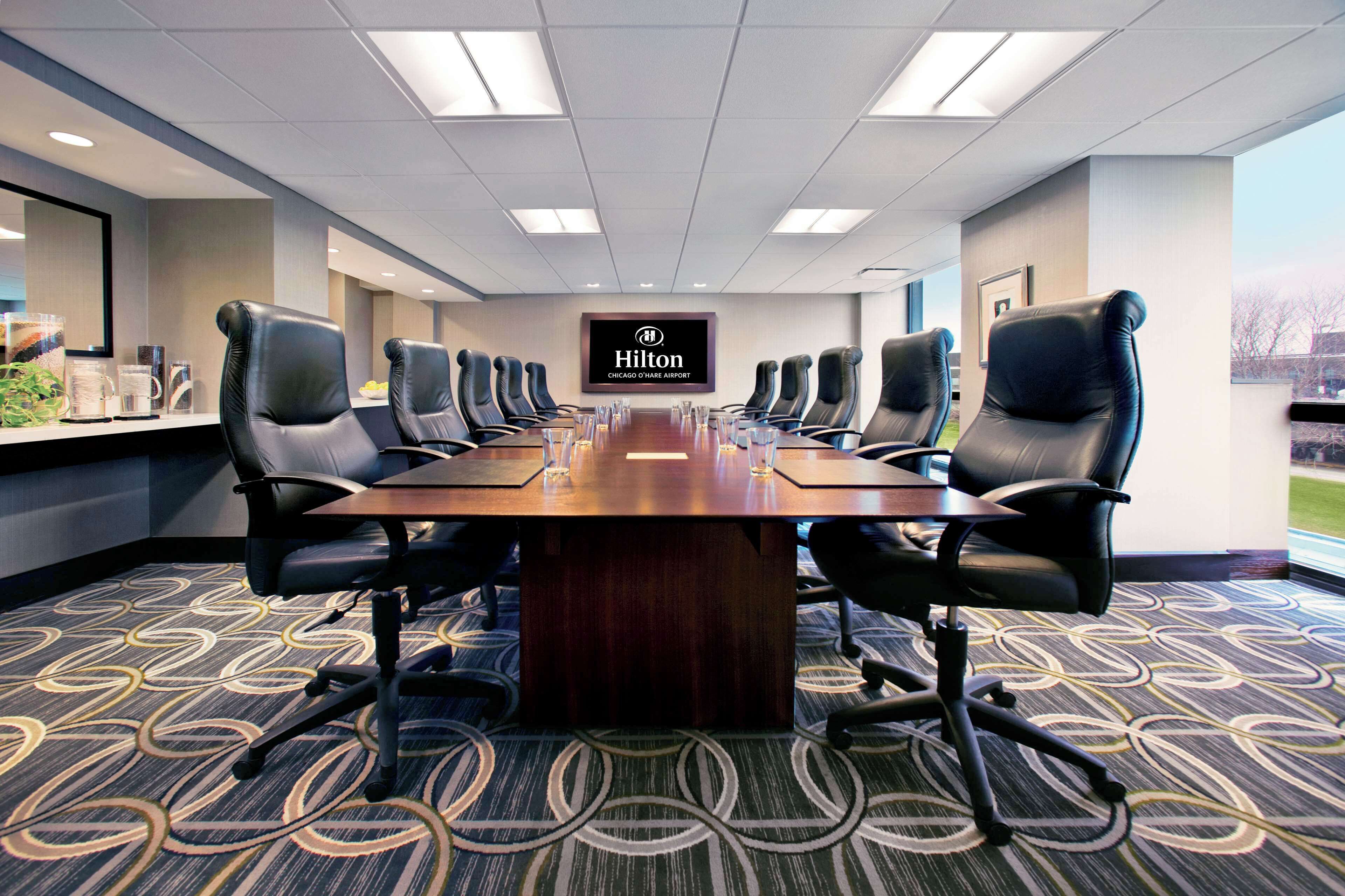 A conference room with a long table, multiple chairs, and a Hilton logo on the wall.