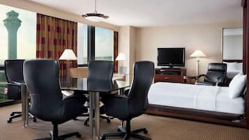 A hotel room with a large bed, two black office chairs, a desk with a lamp, a television, and a view of a tower.