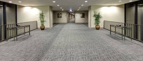 Un pasillo de hotel con pisos alfombrados, barandales de metal y plantas en macetas.