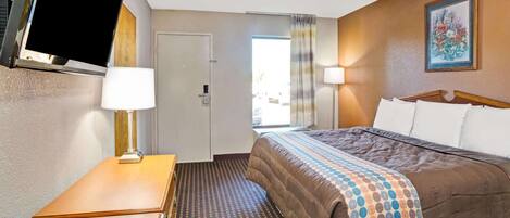 Una habitación de hotel con cama, escritorio, televisor y puerta.