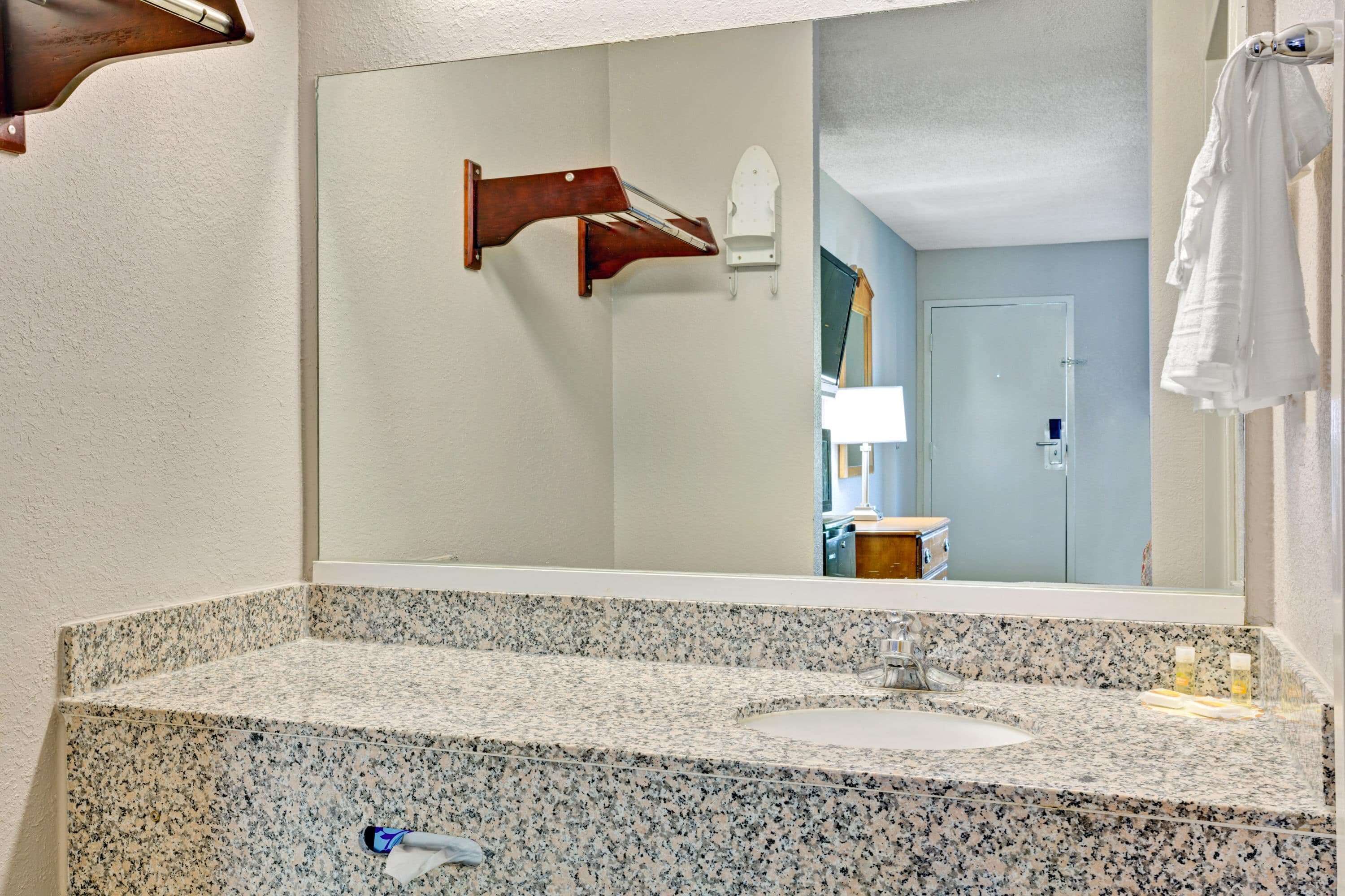 A bathroom with a granite countertop sink, a large mirror, and a towel rack.