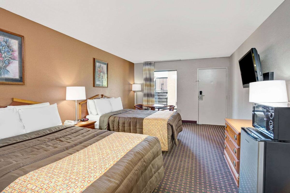 A hotel room with two beds, a desk with a television, and a door leading to a balcony.