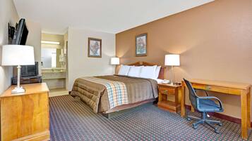 A hotel room with a bed, desk, chair, lamps, and a television.