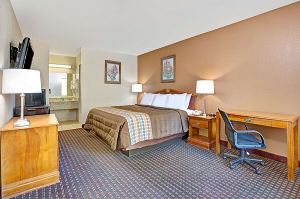 Una habitación de hotel con cama, escritorio, silla, lámparas y televisión.