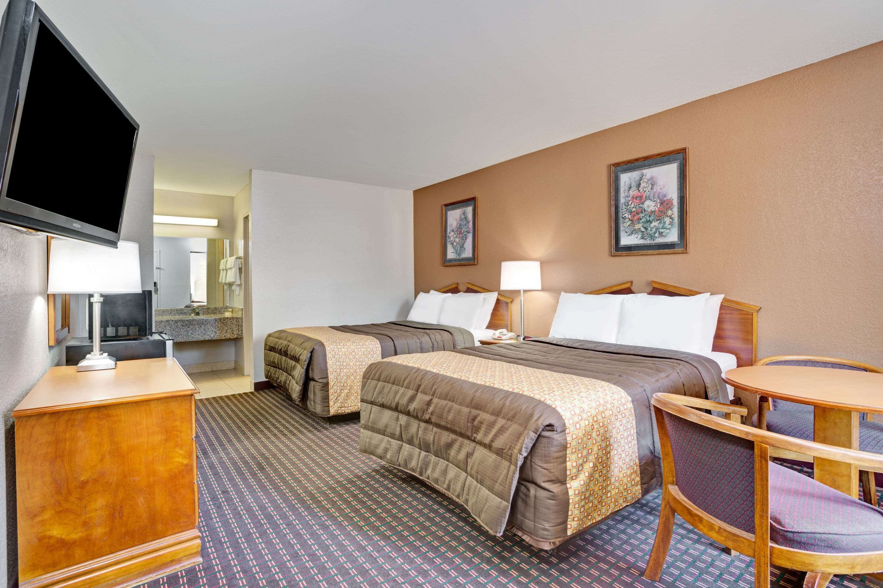 A hotel room with two beds, a desk, a chair, a television, and artwork on the walls.