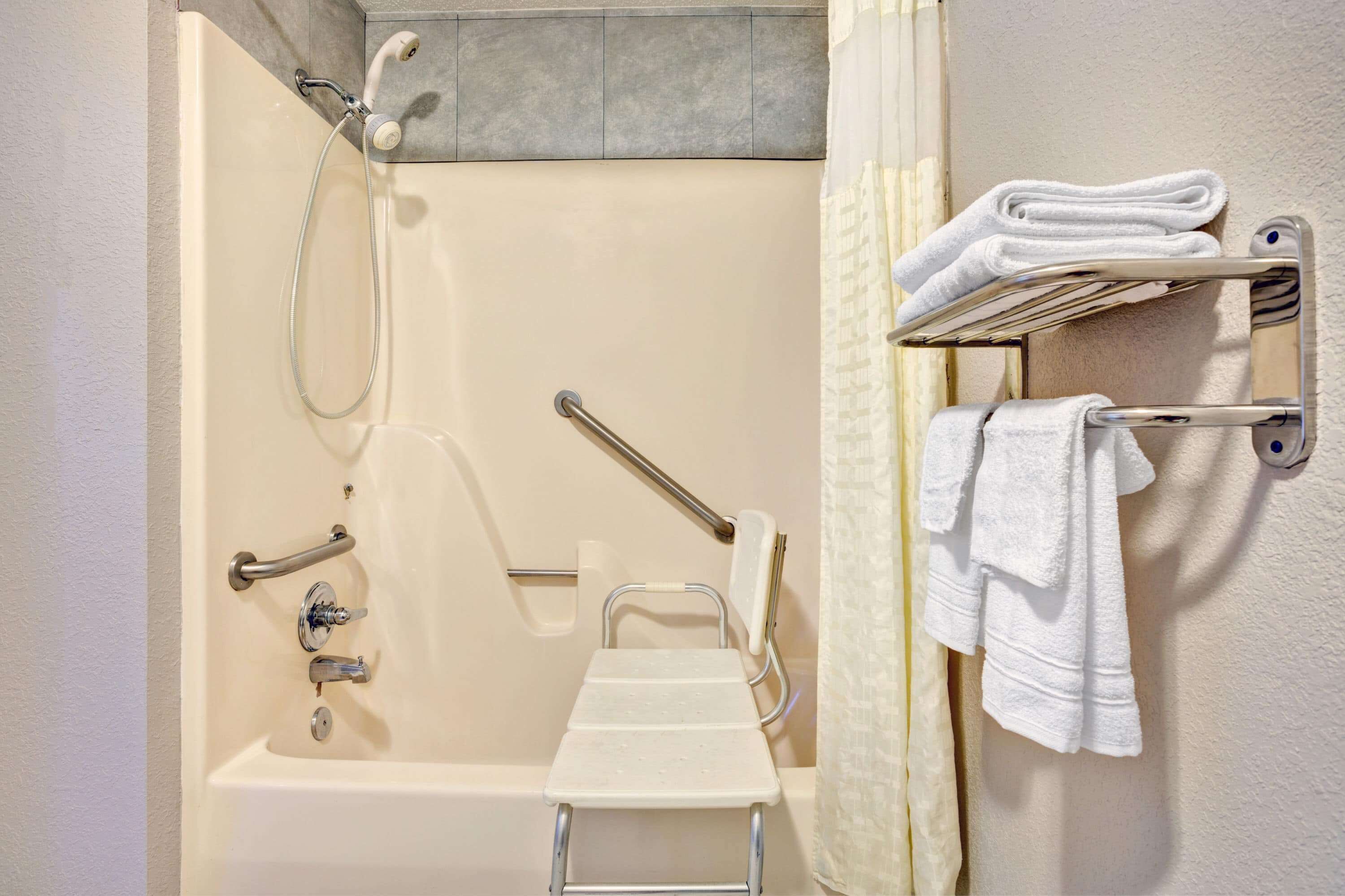 A bathroom with a bathtub, grab bars, a showerhead, and a towel rack with folded towels.