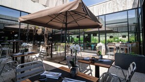 An outdoor dining area with tables and chairs, a large umbrella, and a view of the building's exterior.