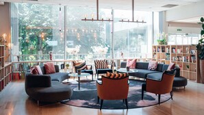 A modern library with large windows, comfortable seating, and a variety of bookshelves.