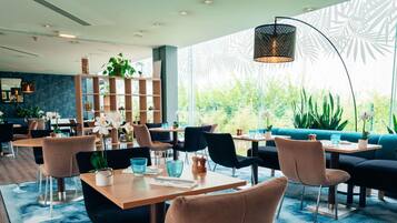 Un restaurant moderne avec des tables rondes, des chaises rembourrées et une grande fenêtre donnant sur un paysage verdoyant.