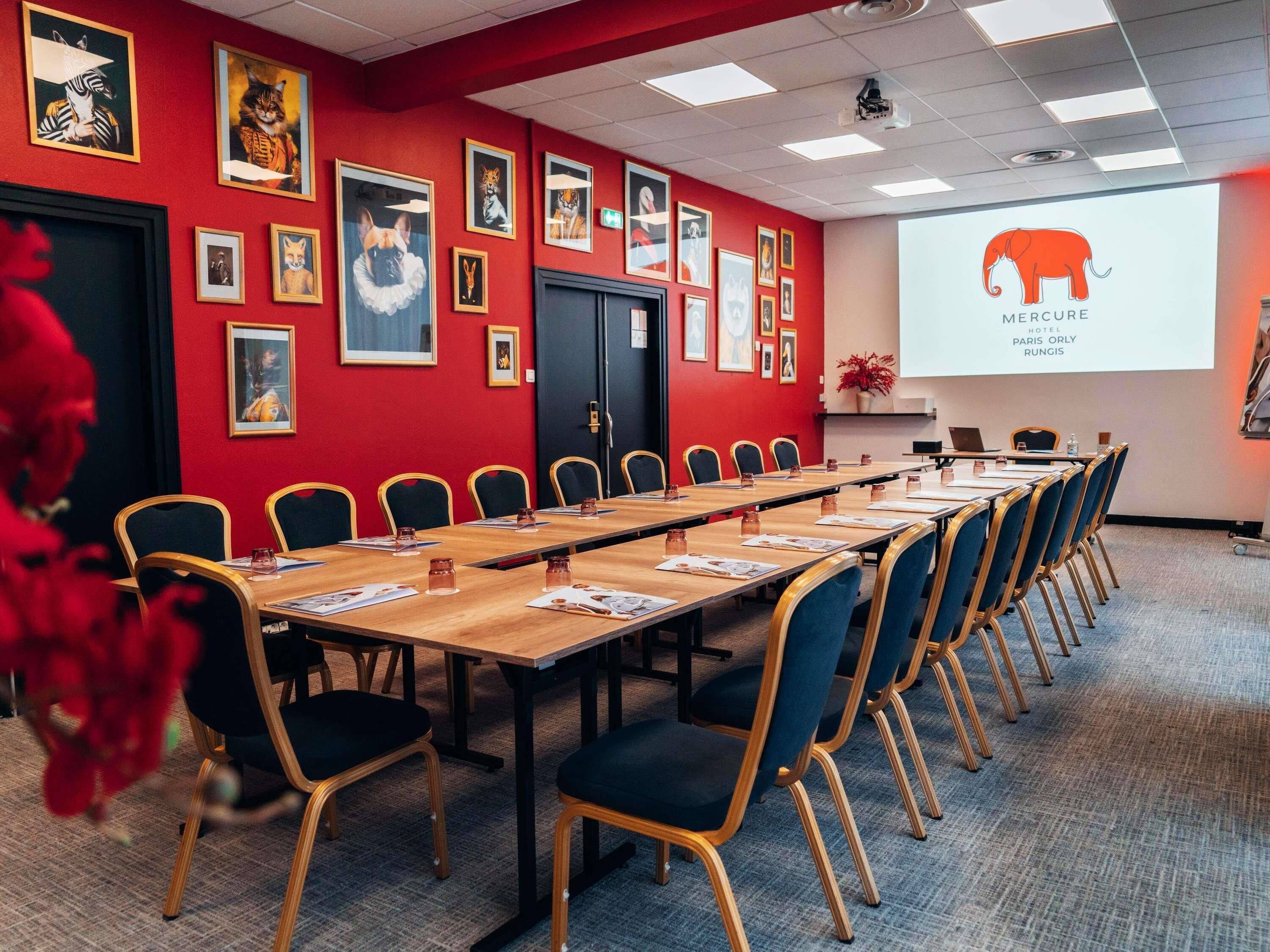 A conference room with a long table, chairs, and a projector screen displaying a logo.