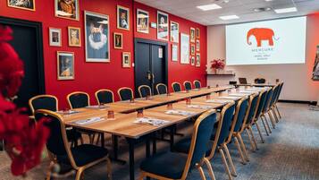 A conference room with a long table, chairs, and a projector screen displaying a logo.