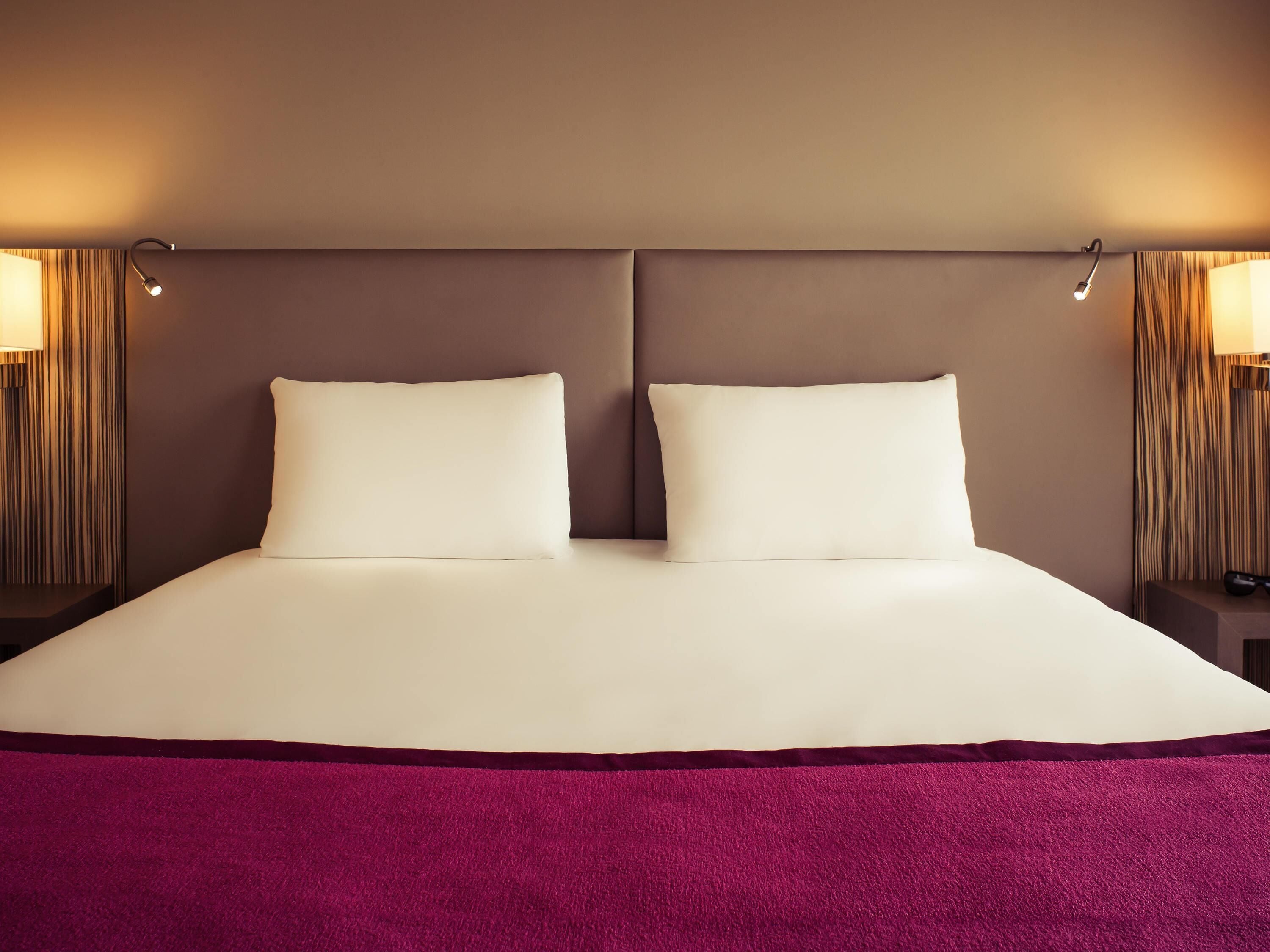 A double bed with a purple throw blanket, two bedside lamps, and a headboard.