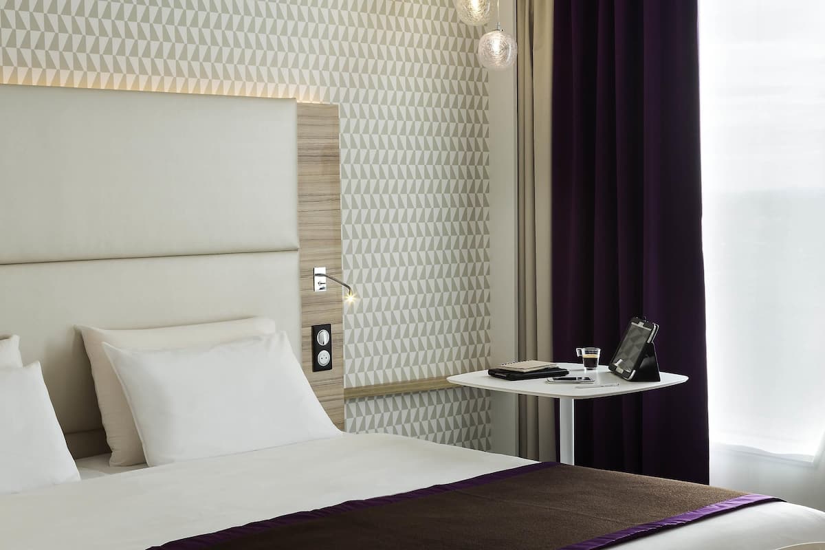 A hotel room with a bed, bedside table, and a wall with geometric patterns.