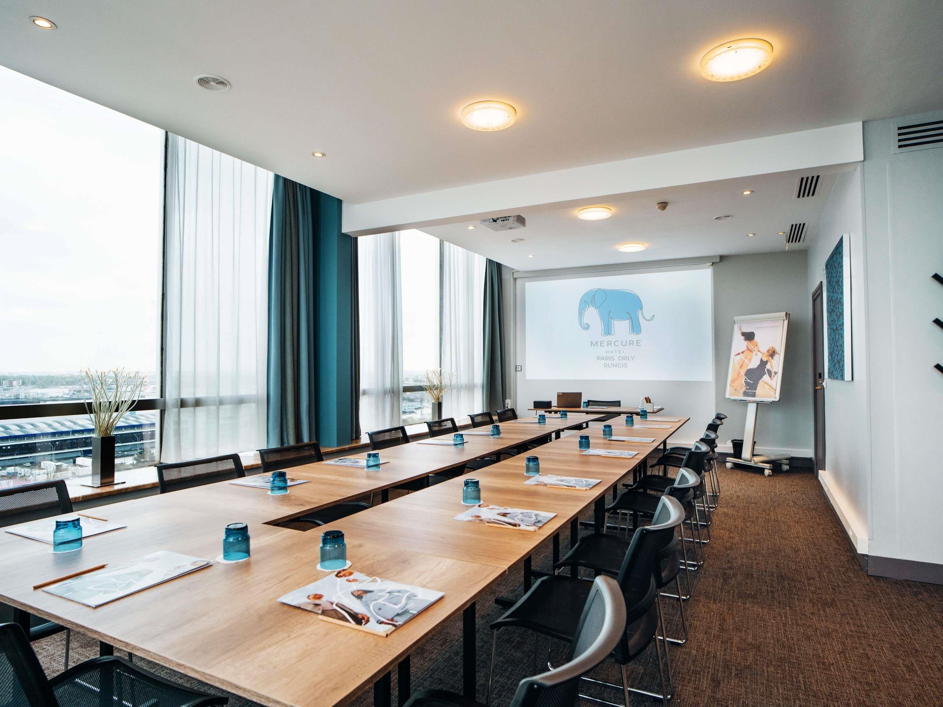 A conference room with a long table, chairs, a projector screen, and a view of the city.