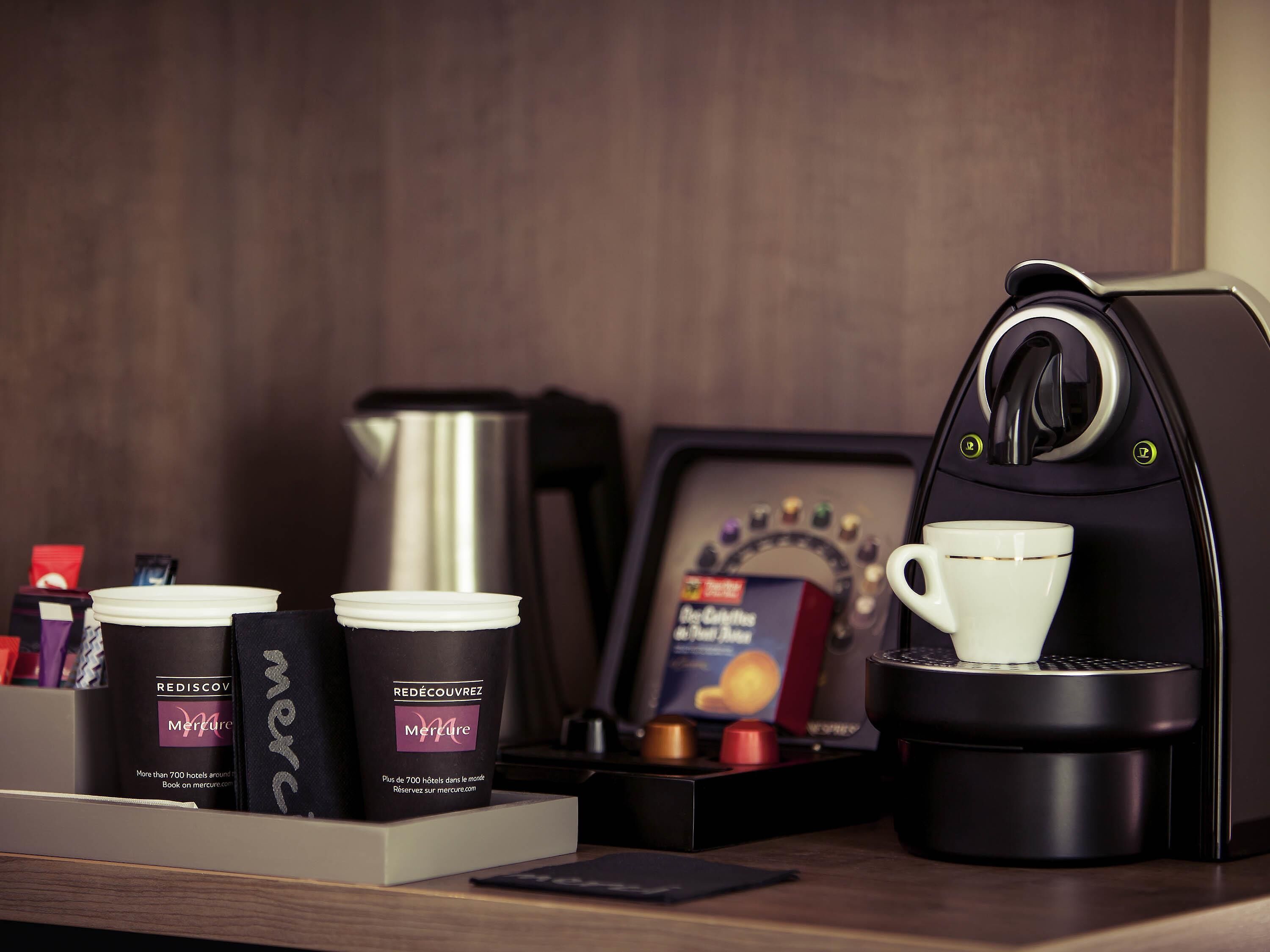 A coffee machine, two coffee cups, a thermos, and a framed menu on a wooden table.