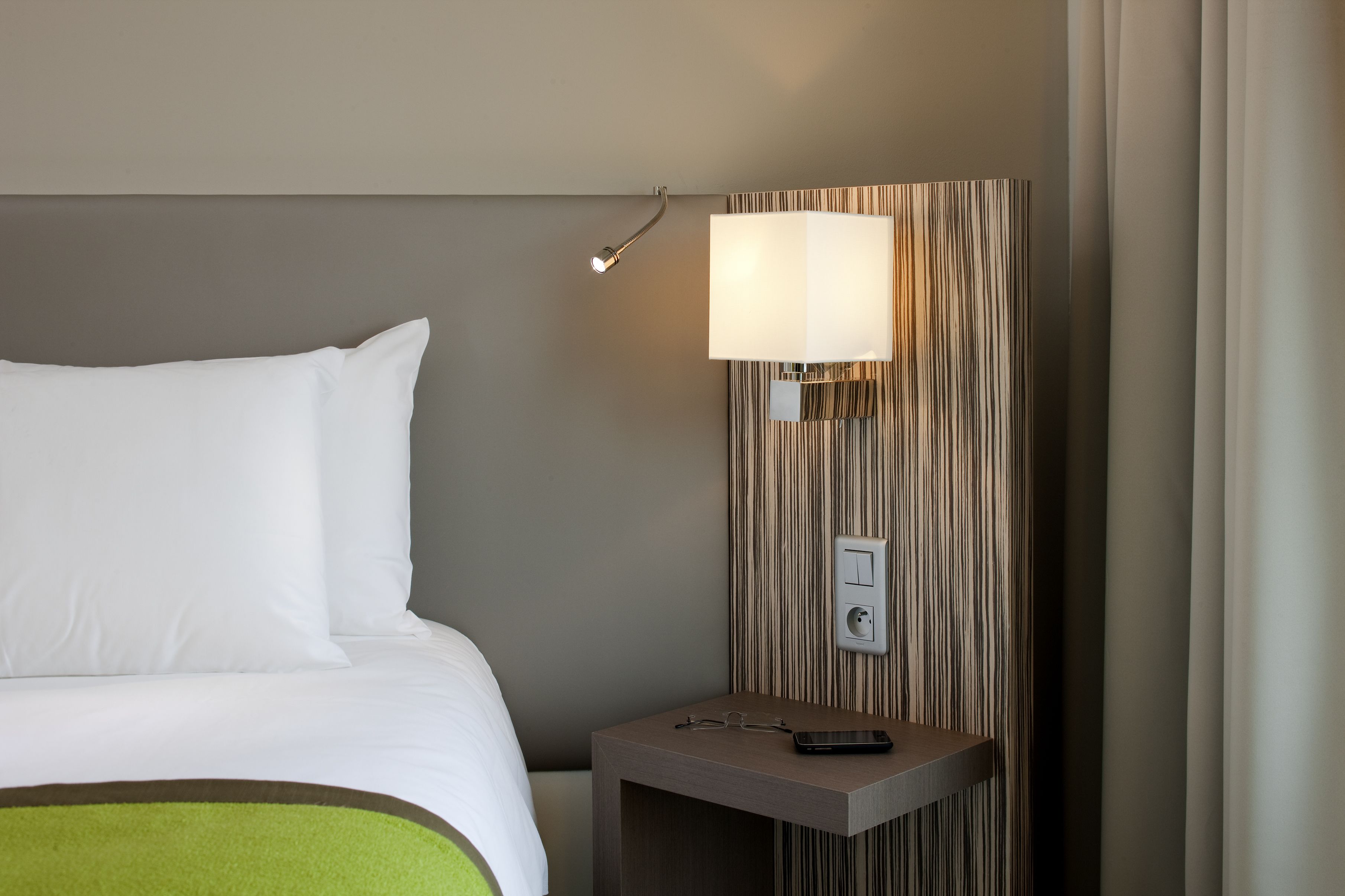 Habitación de hotel con una cama, una mesita de noche con lámpara e interruptor en la pared.