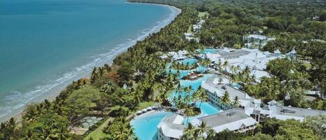 An aerial view of a resort with a large pool, beachfront, and lush greenery.