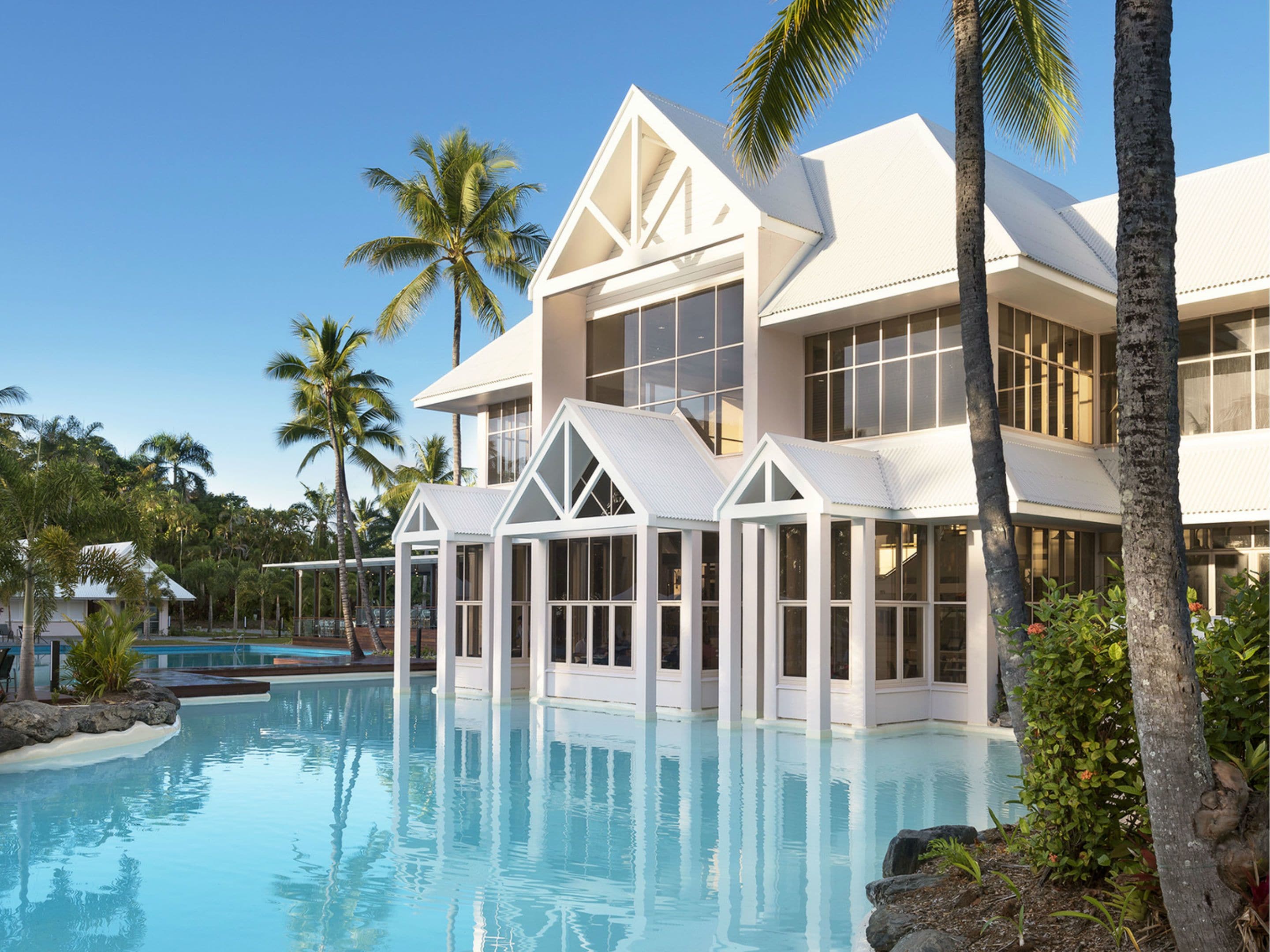 A modern resort with a pool, white architecture, and palm trees.