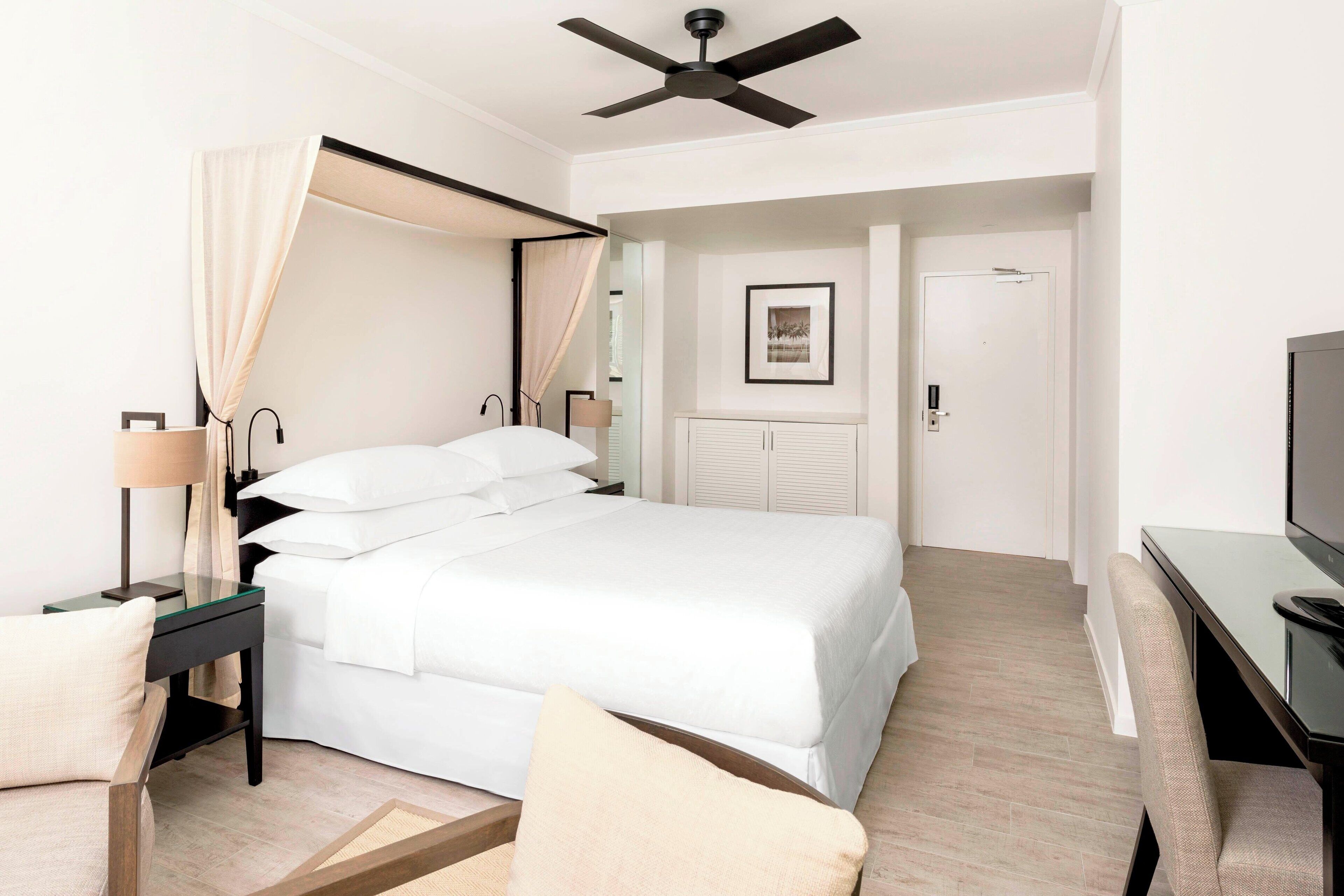 A modern hotel room with a bed, bedside table, lamp, and a television.