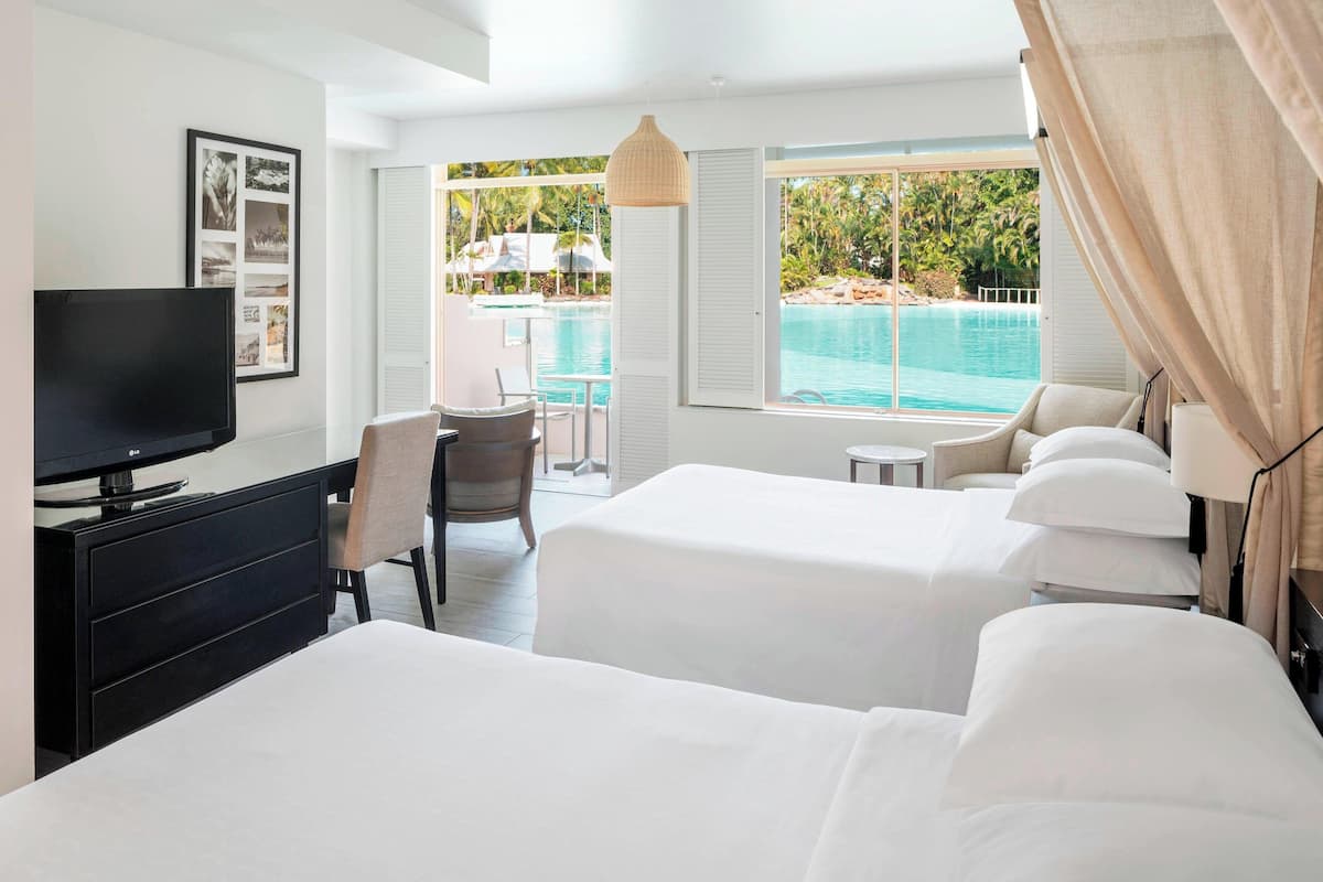 Habitación de hotel con dos camas, televisión, escritorio y vista a una piscina.