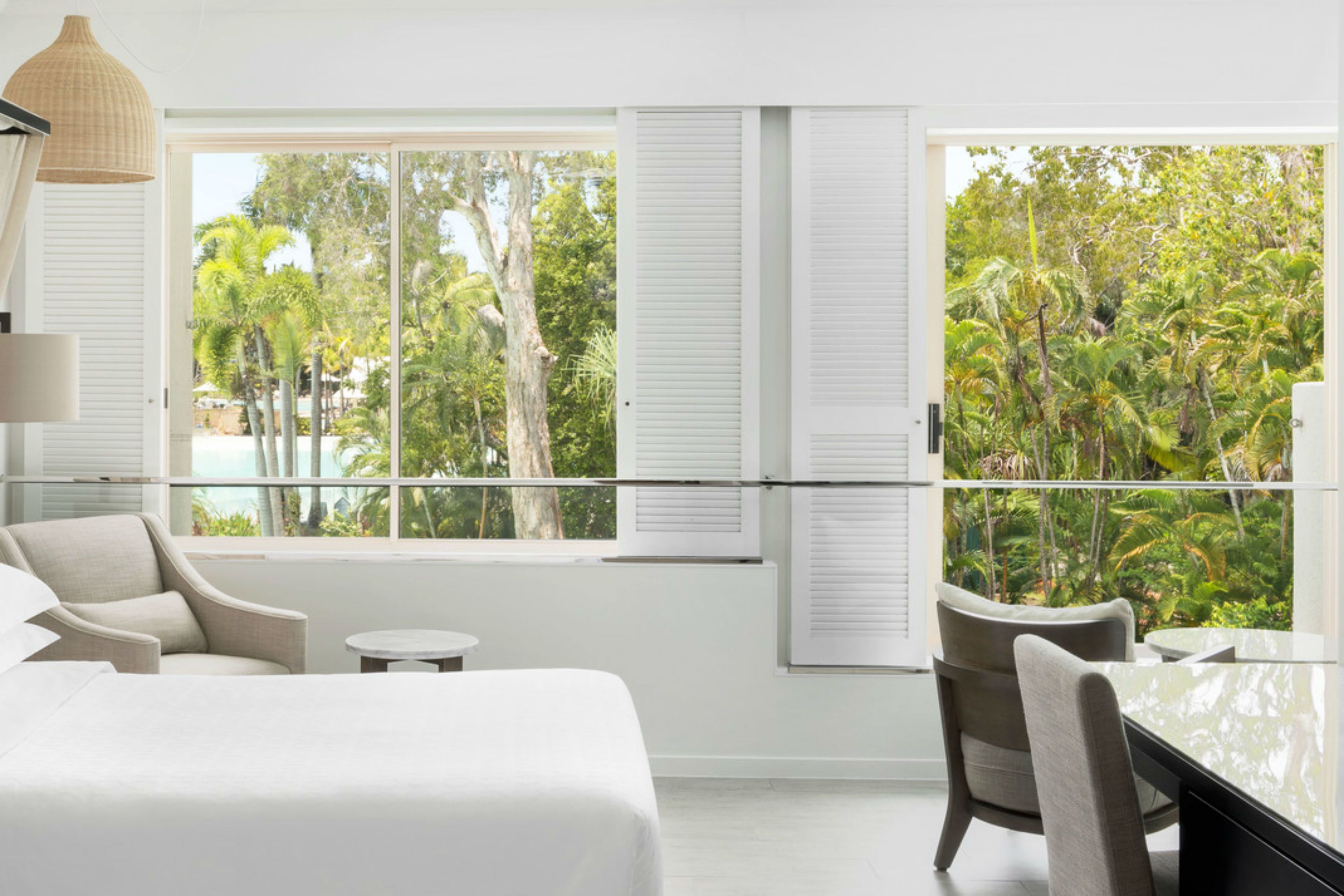 Habitación de hotel moderna con una cama grande, una pequeña mesa redonda, una silla y un balcón con vistas a vegetación exuberante.