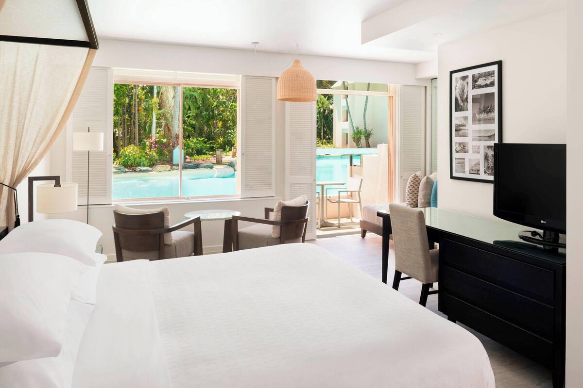 Habitación de hotel con una cama grande, un escritorio, una silla, un televisor y vista a una piscina.