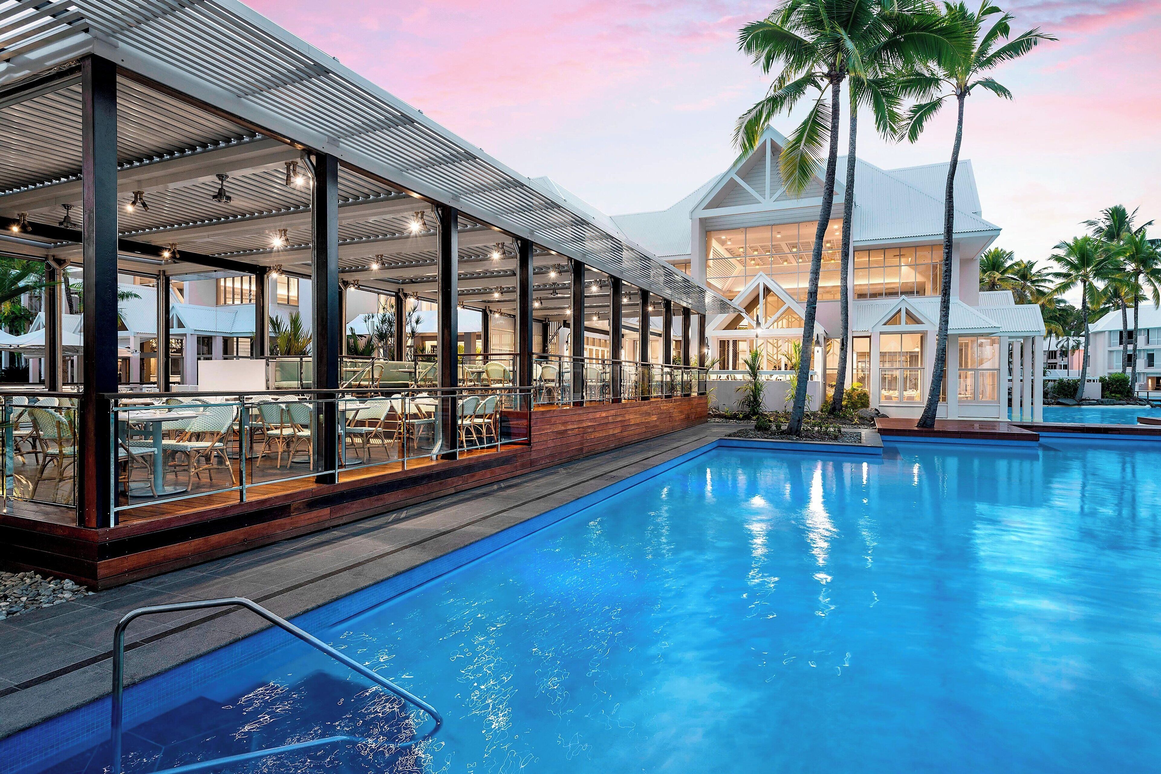 A modern hotel with a pool, outdoor seating, and a large building with large windows.