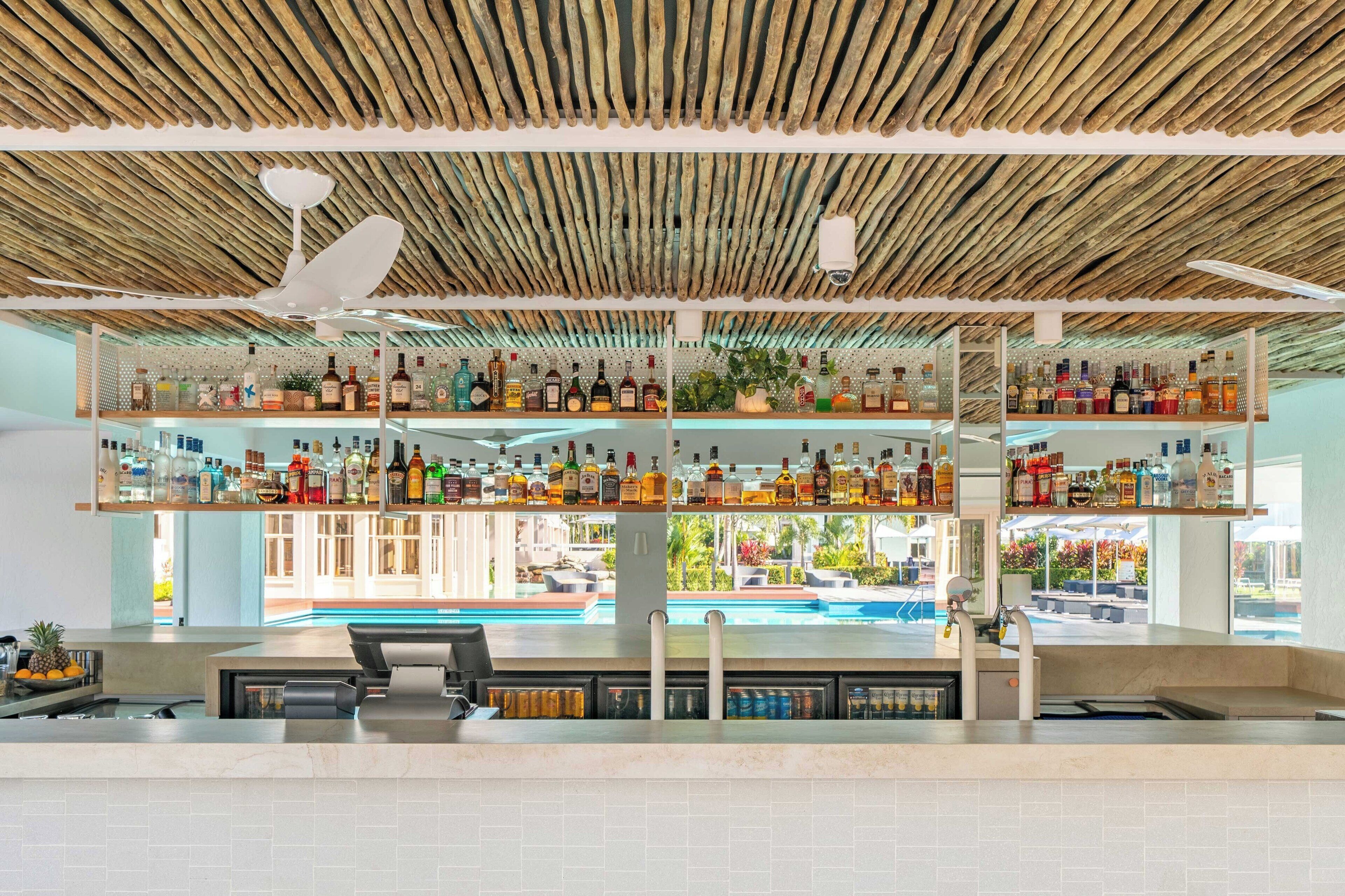 A bar with multiple shelves of liquor bottles, a ceiling fan, and a view of an outdoor pool area.