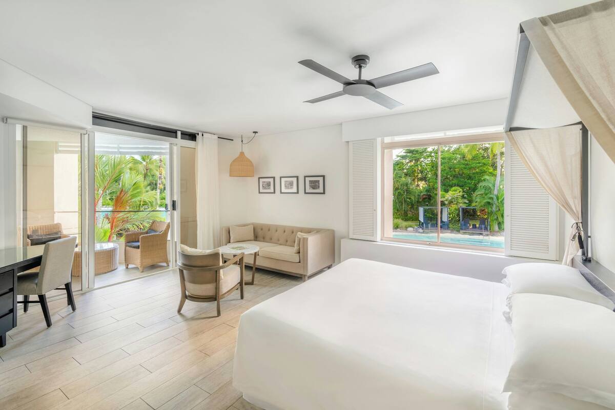 Habitación de hotel con cama, escritorio, silla, sofá y vista a una piscina.
