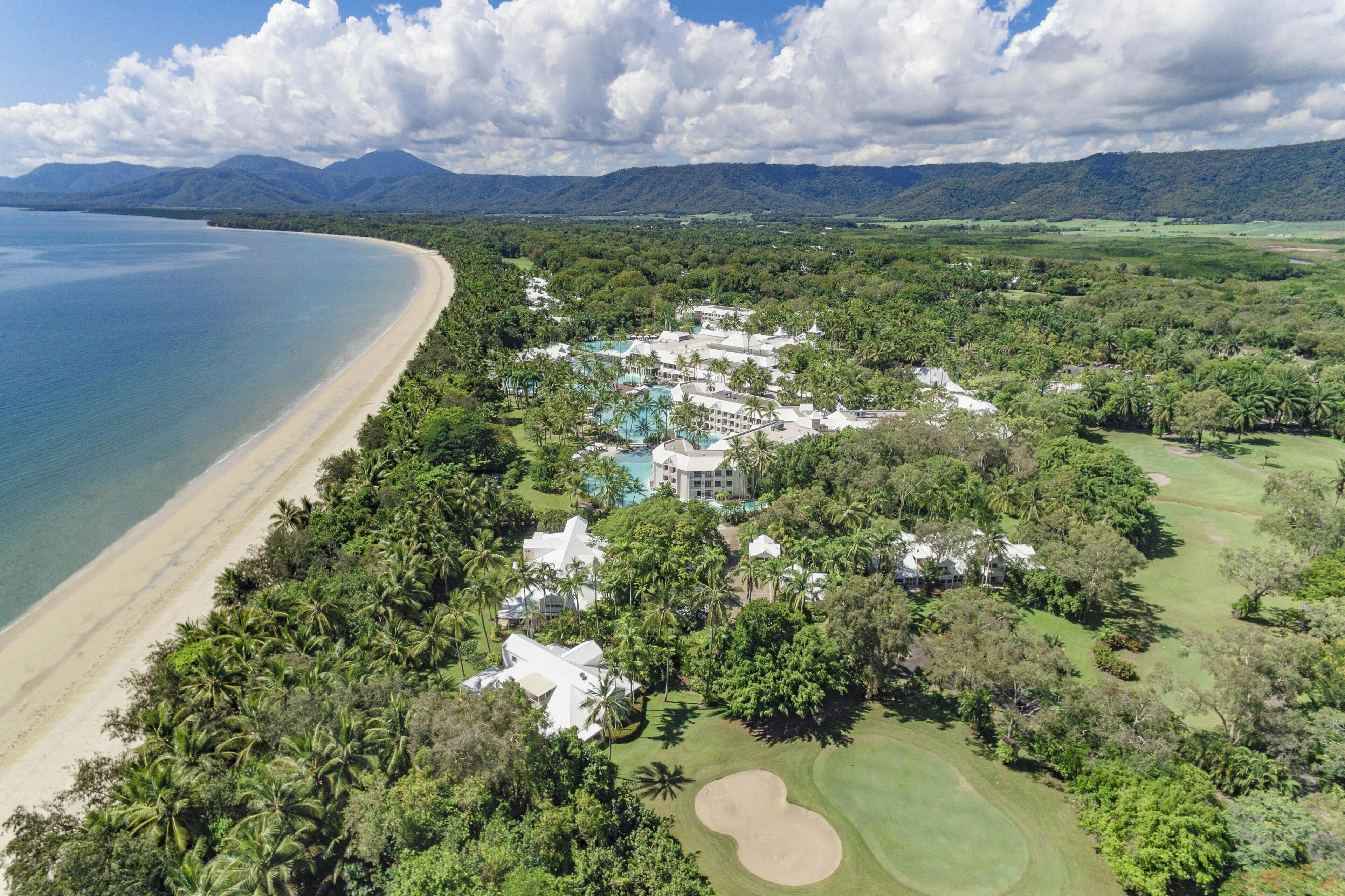 An aerial view of a resort with a beach, lush greenery, and a golf course.