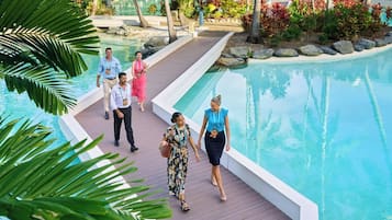 Un área junto a la piscina con terraza de madera, palmeras y una piscina azul cristalina.