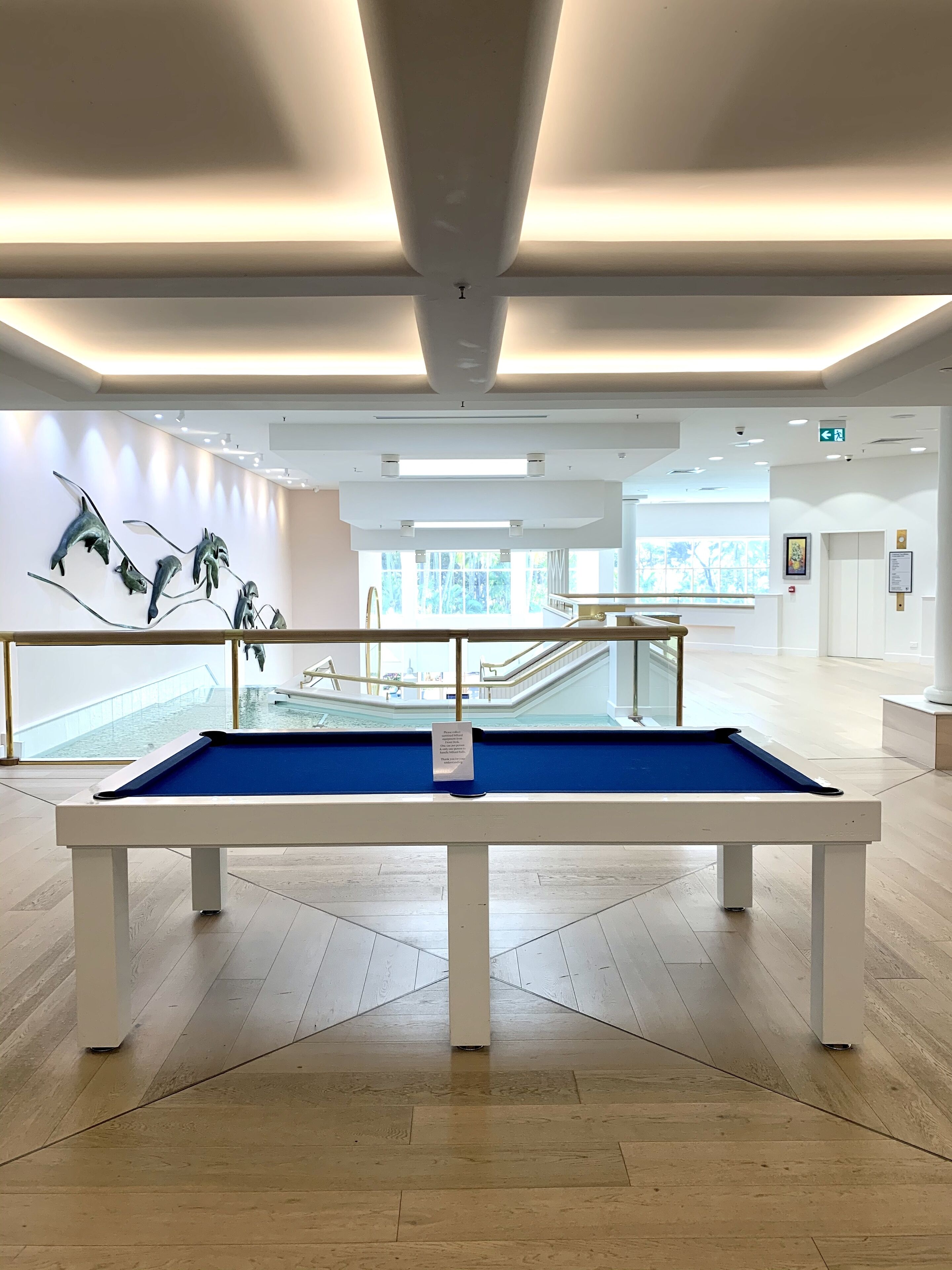 A pool table in a spacious, well-lit room with a modern design, large windows, and a view of a pool area.