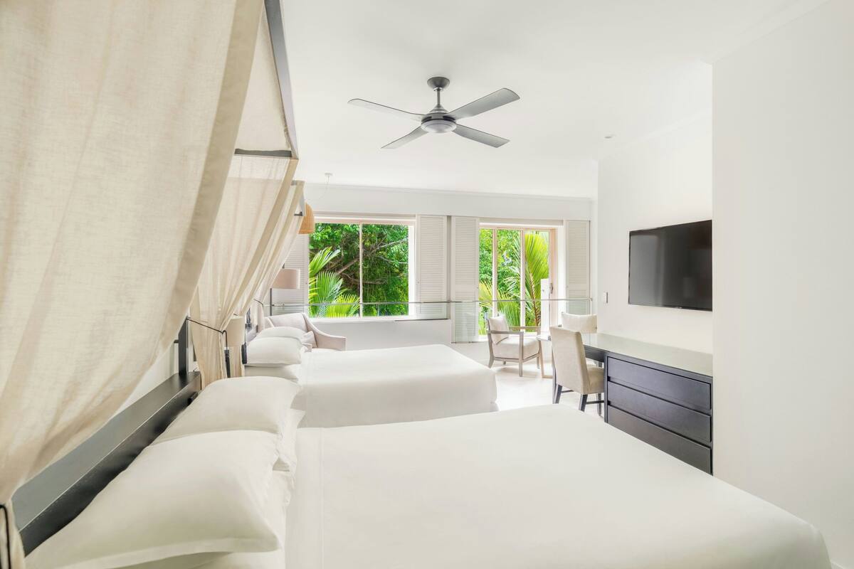 Una habitación de hotel con cama, escritorio, silla, televisor y ventilador de techo.