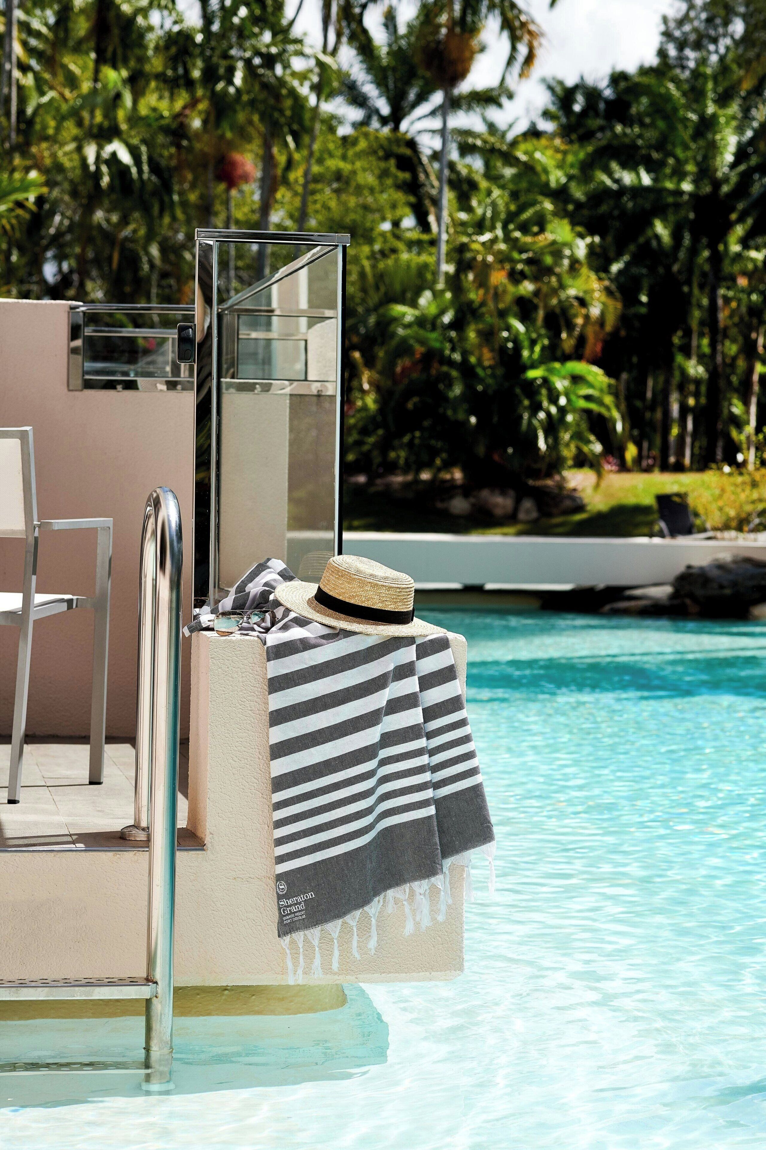 A poolside area with a metal chair, a towel, and a straw hat on a bench.
