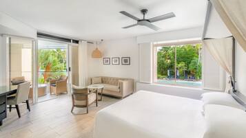 Ein Hotelzimmer mit Bett, Schreibtisch, Sessel, Sofa, Deckenventilator und einem Fenster mit Blick auf Grünflächen.