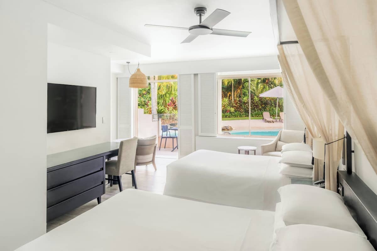 Habitación de hotel con cama, escritorio, televisor y vistas a una piscina y jardín.
