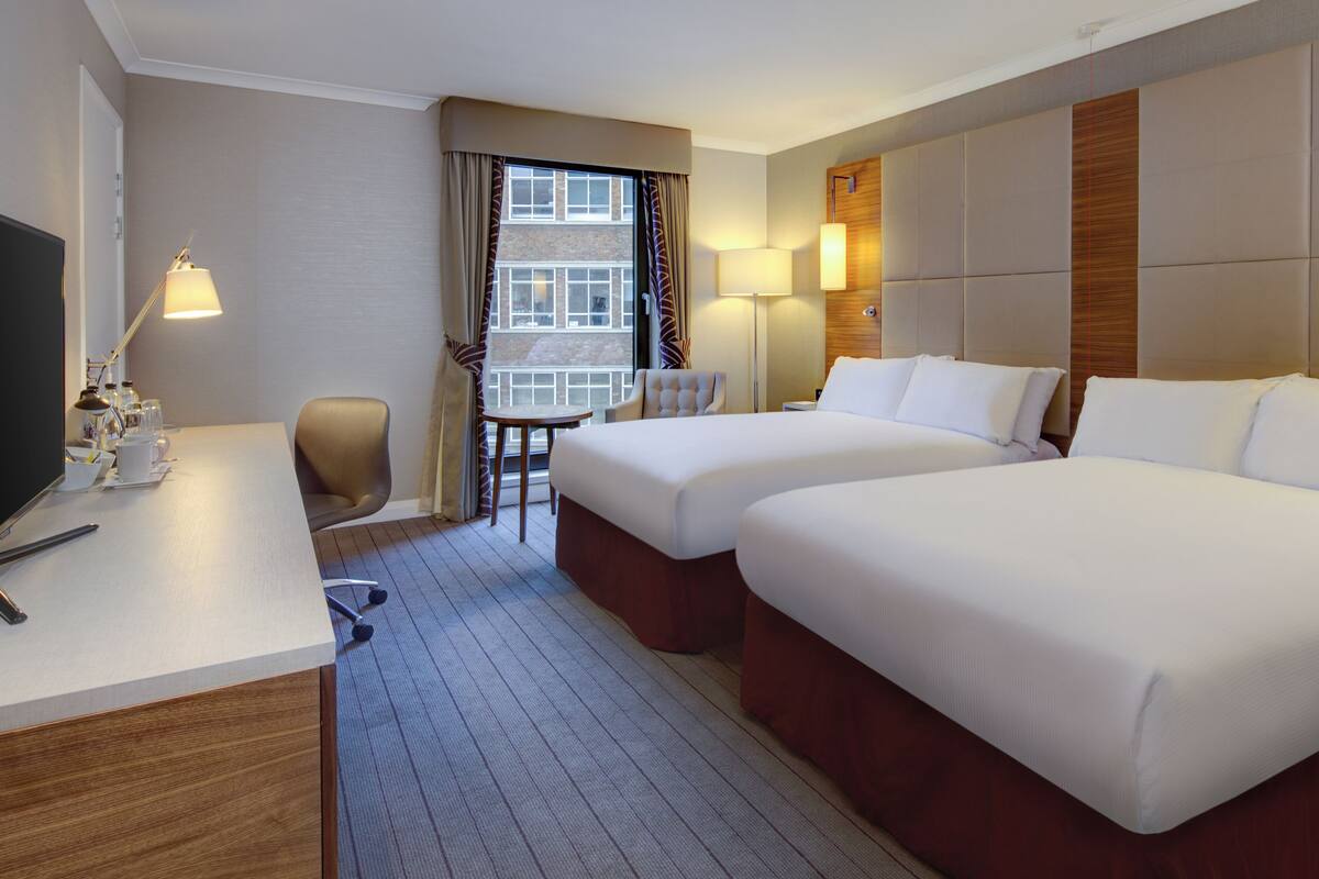 Habitación de hotel con dos camas, un escritorio, una silla y un televisor.