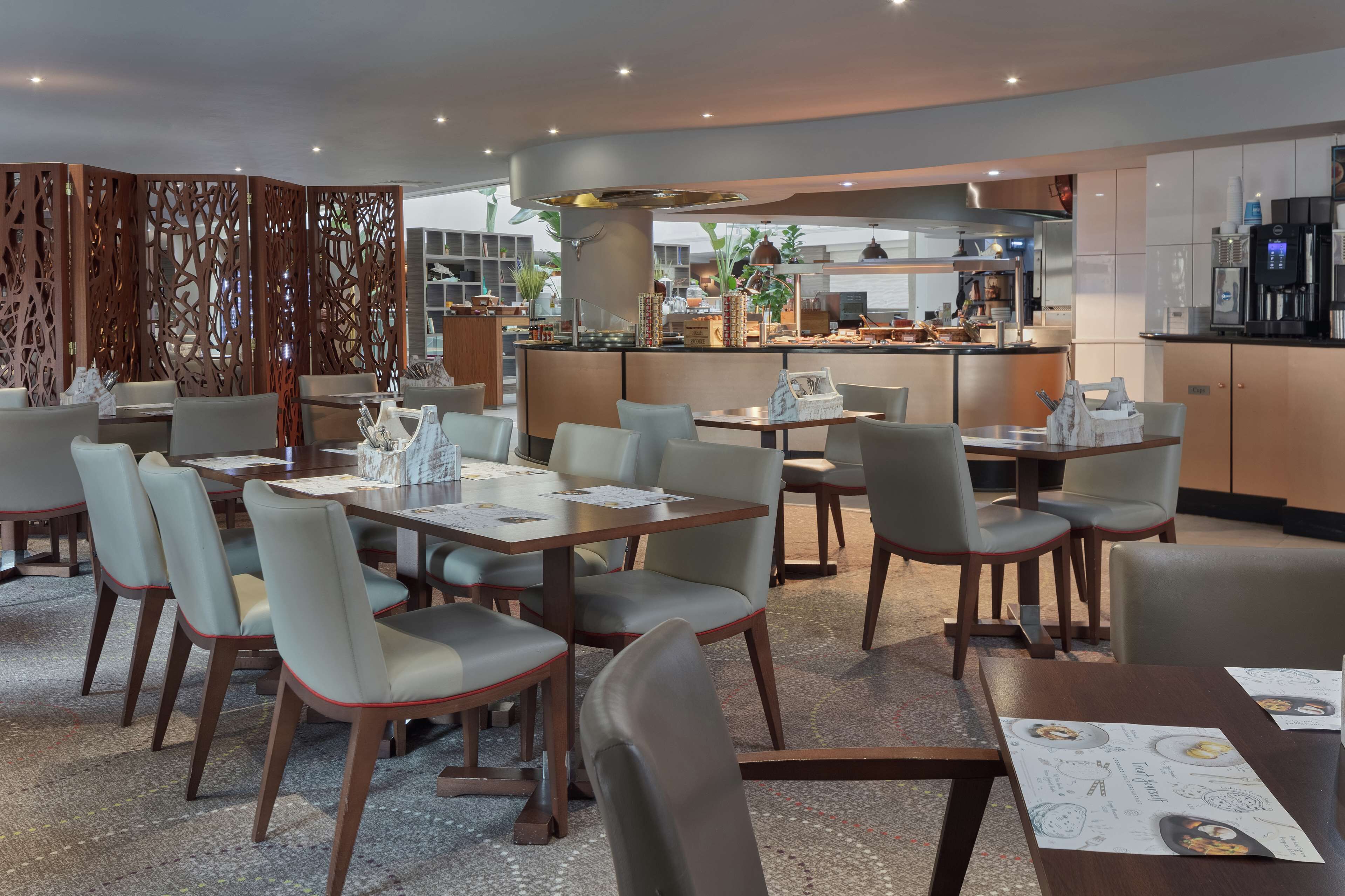 A modern restaurant with multiple dining tables and chairs, a kitchen area, and a decorative partition.