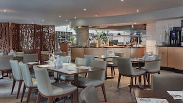 A modern restaurant with multiple dining tables and chairs, a kitchen area, and a decorative partition.