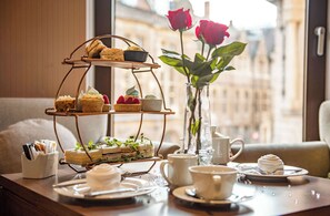 A tiered dessert stand with various pastries and sandwiches, a vase with roses, and a table set with cups and plates. - Hilton Cambridge City Centre (Cambridge)